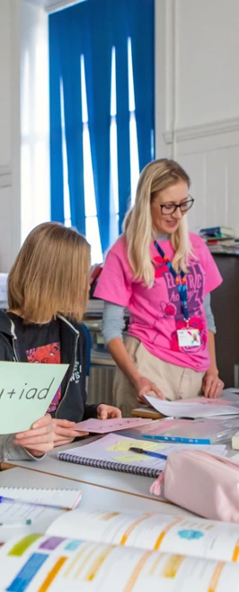 Gaelic lecturer supporting students in a language learning activity, with students holding vocabulary cards and engaging in conversation. Gaelic lecturer supporting students in a language learning activity, with students holding vocabulary cards and engaging in conversation.